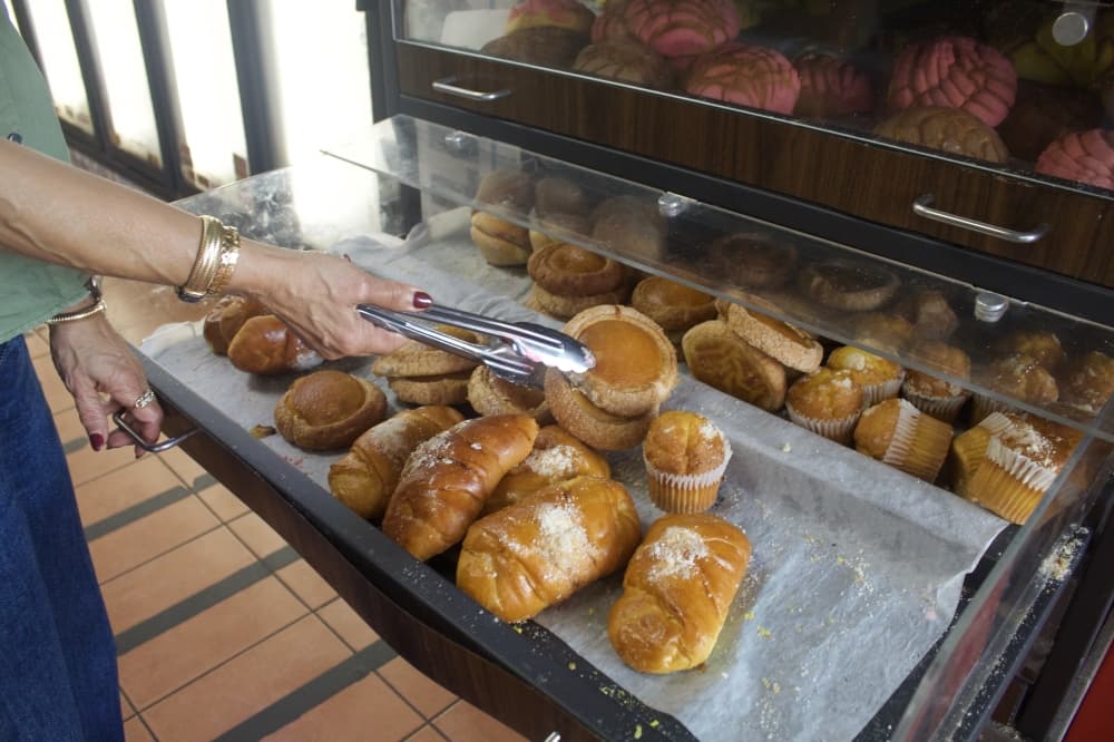 Tongs holding an ojo de buey pastry above a plastic case
