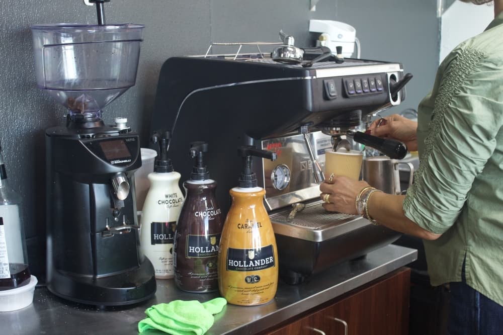 Summer Bannat pulls an espresso shot next to large bottles of flavored syrup