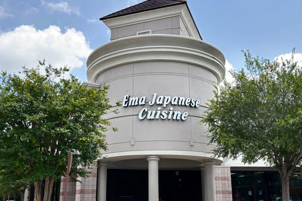 Exterior view of Ema Japanese Cuisine's building, surrounded by green trees on both sides