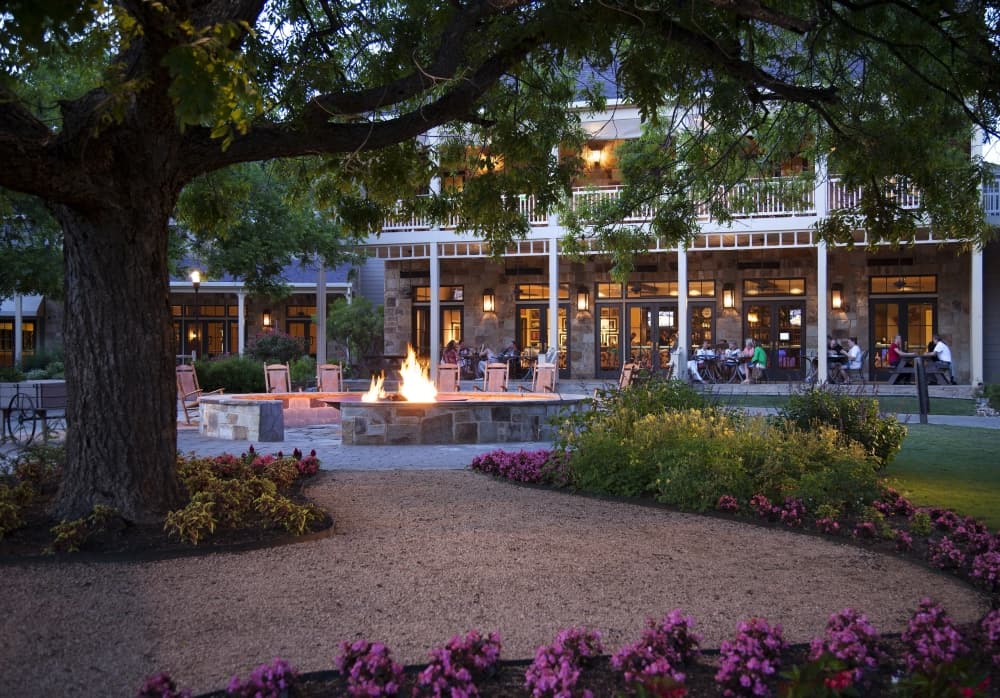 Hyatt Regency Lost Pines Resort & Spa’s exterior patio area is shown at dusk with outdoor seating, landscaping and fire pits.