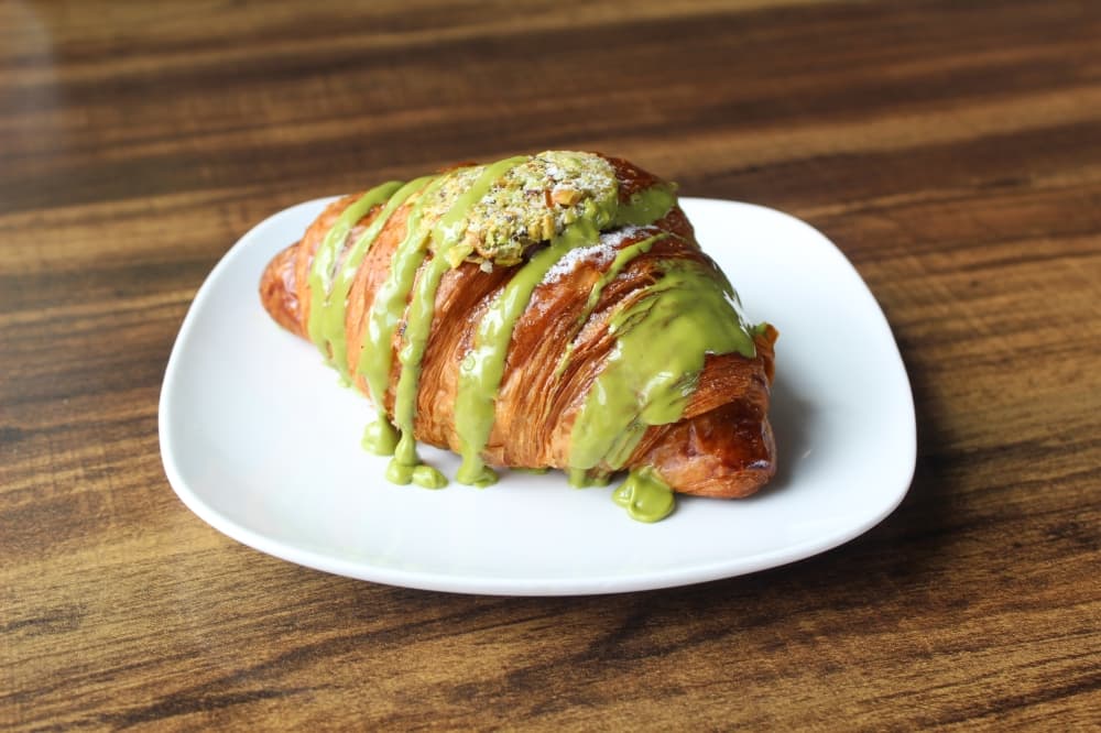 A croissant with green pistachio drizzle on a white plate