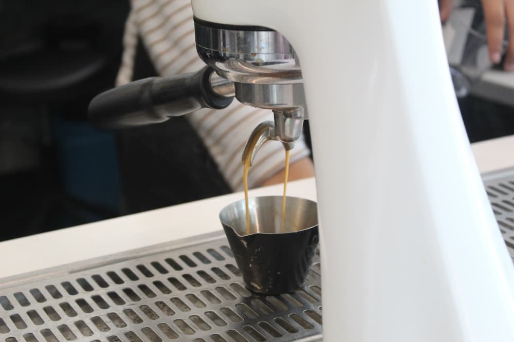 Espresso pours into a small cup from a sleek white spout