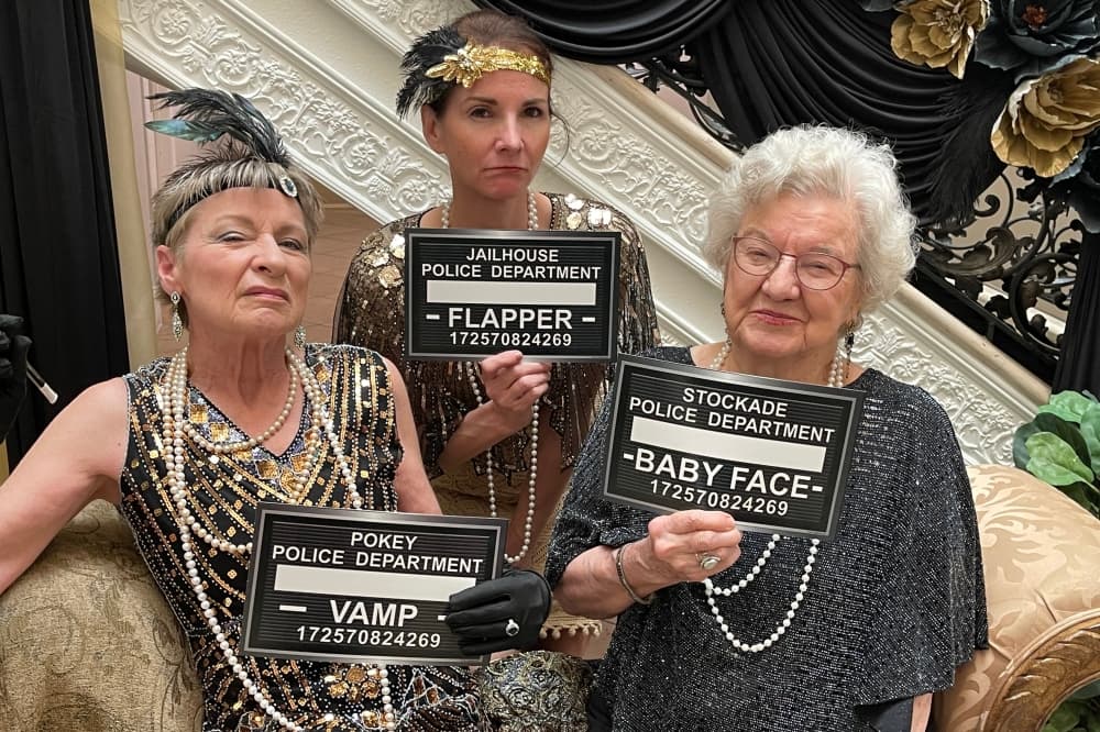 Three women dressed in Roaring 20s Attire, each of them are holding up inmate signs that describe who they are dressed as