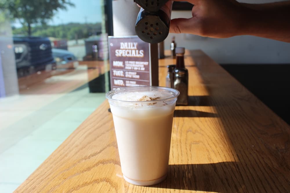 Cinnamon sprinkles onto a clear plastic cup of horchata