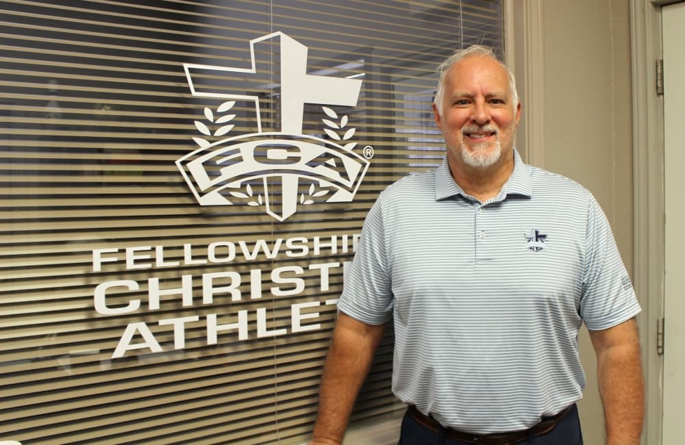 Jamie Clark standing to the right of FCA's logo embossed onto a window