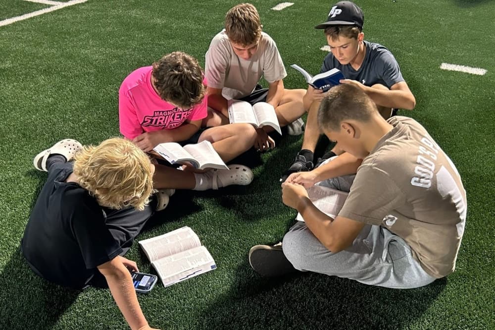 A group of boys in the middle of their Bible study, they are seated in a circle on a football field
