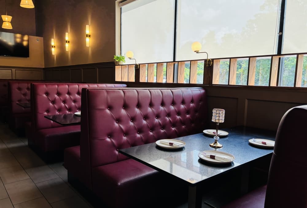 Interior view of Curry & Grill, there are two booths lined with plum leather seating and black tables, the tables are plated with dishes and silverware