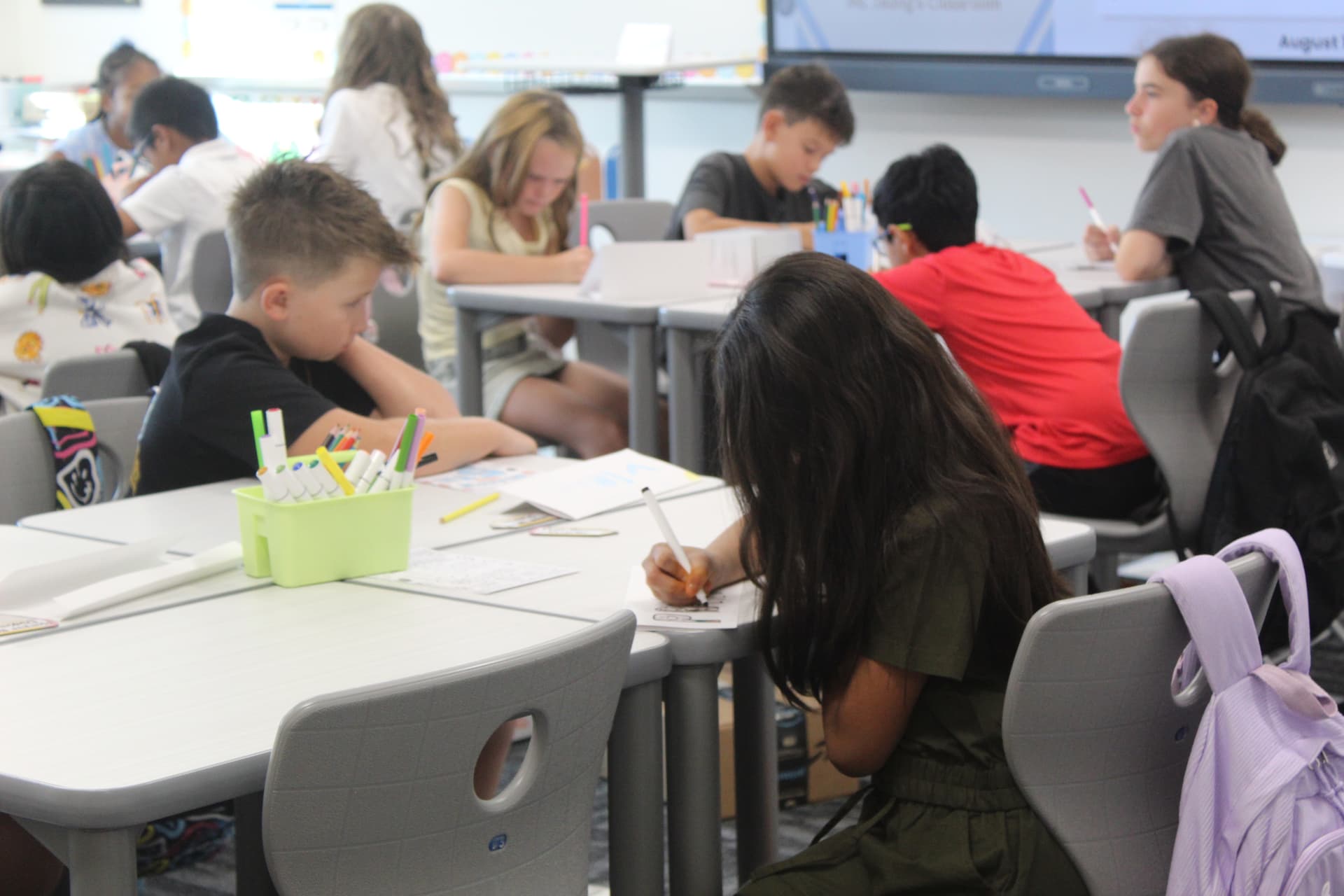 A purple backpack hangs off the chair of a child writing at a table