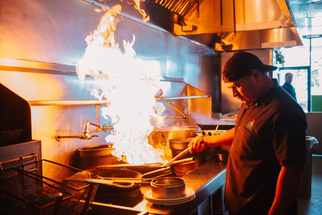 Saba's Grill & Wok chef stir-frying food in a wok, large flames emit from the plan