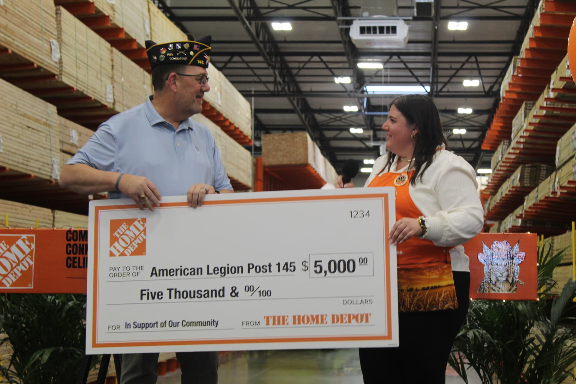 A man in a military hat accepts a large check from a woman in an orange vest