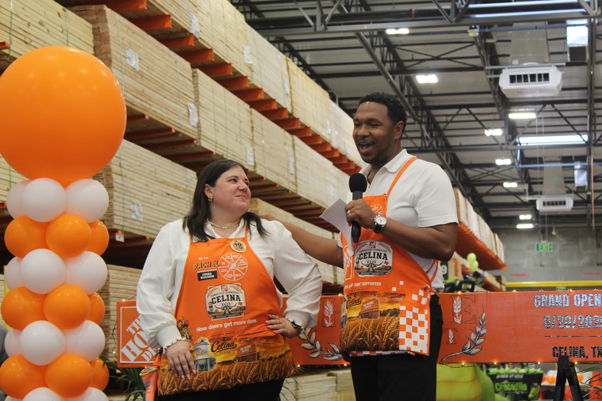 A man and a woman in orange vests on a stage with orange and white balloons