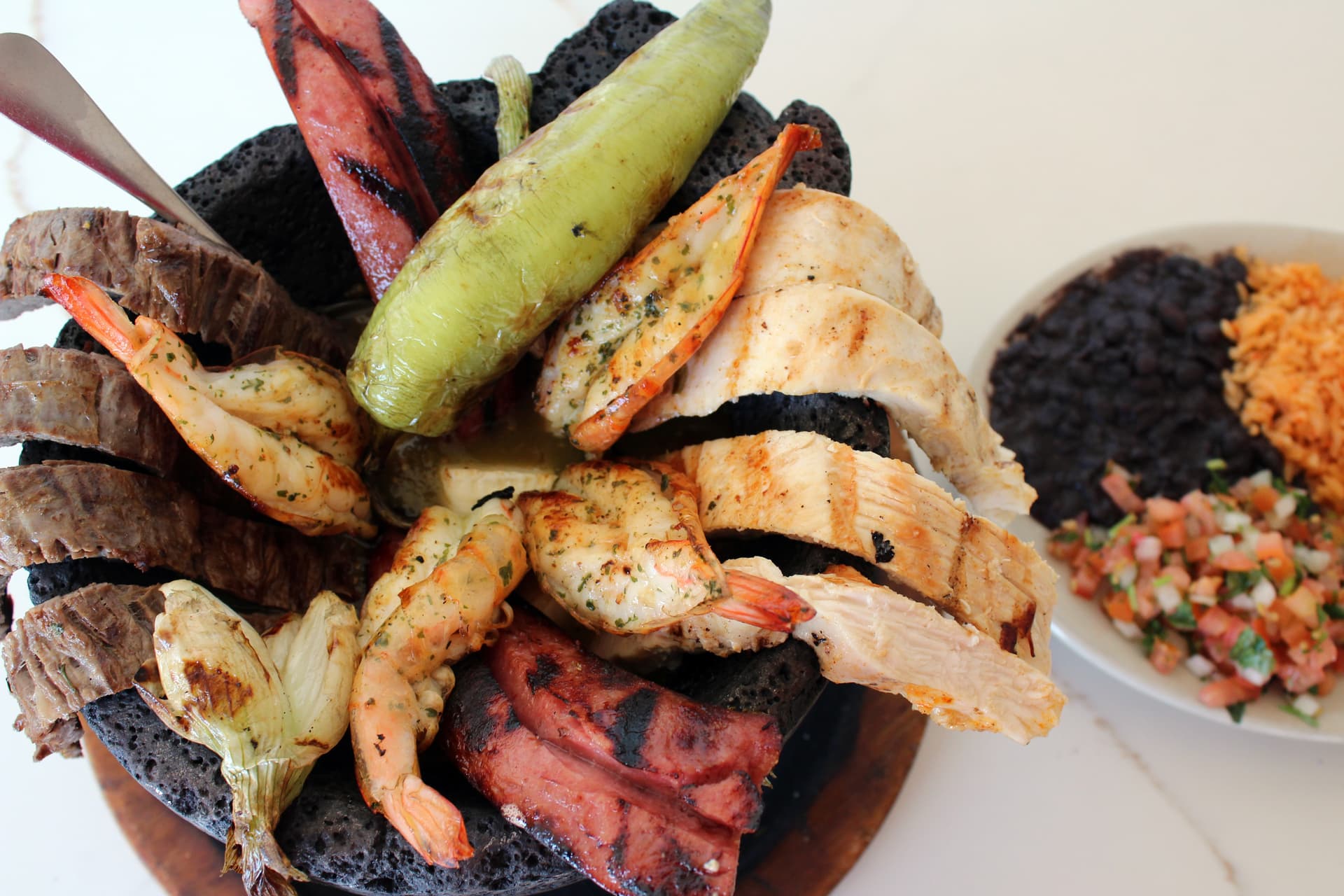 Molcajete ($47 serves two) This dish is served in a carved out lava rock and features salsa verde, panela cheese, beef, chicken fajita, grilled shrimp, sausage and a roasted chile. Served with black beans, rice, pico de gallo and guacamole.