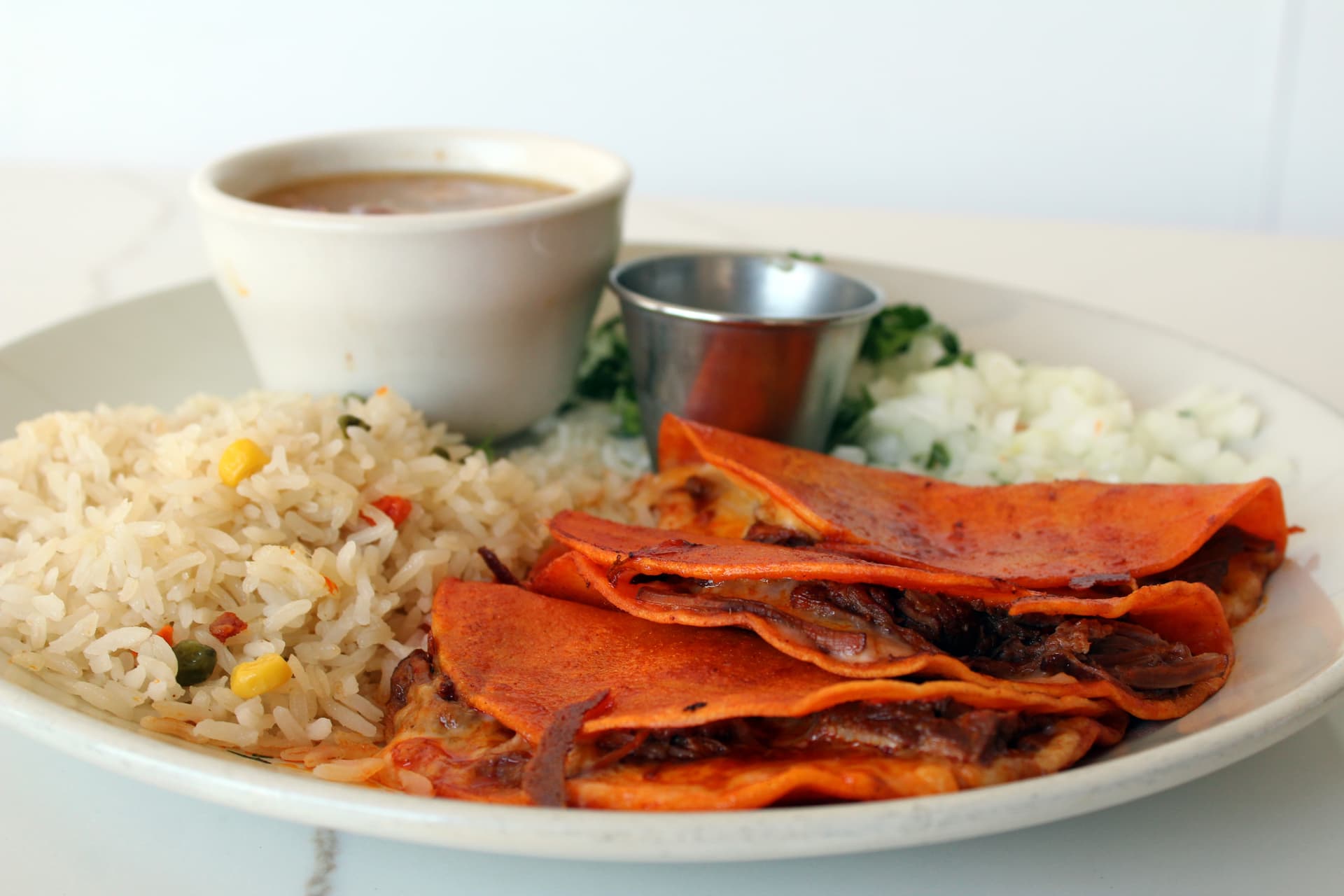 Quesabirrias ($19) features birria-style cooked beef folded into corn tortillas with melted cheese. Served with white rice, onions and cilantro.