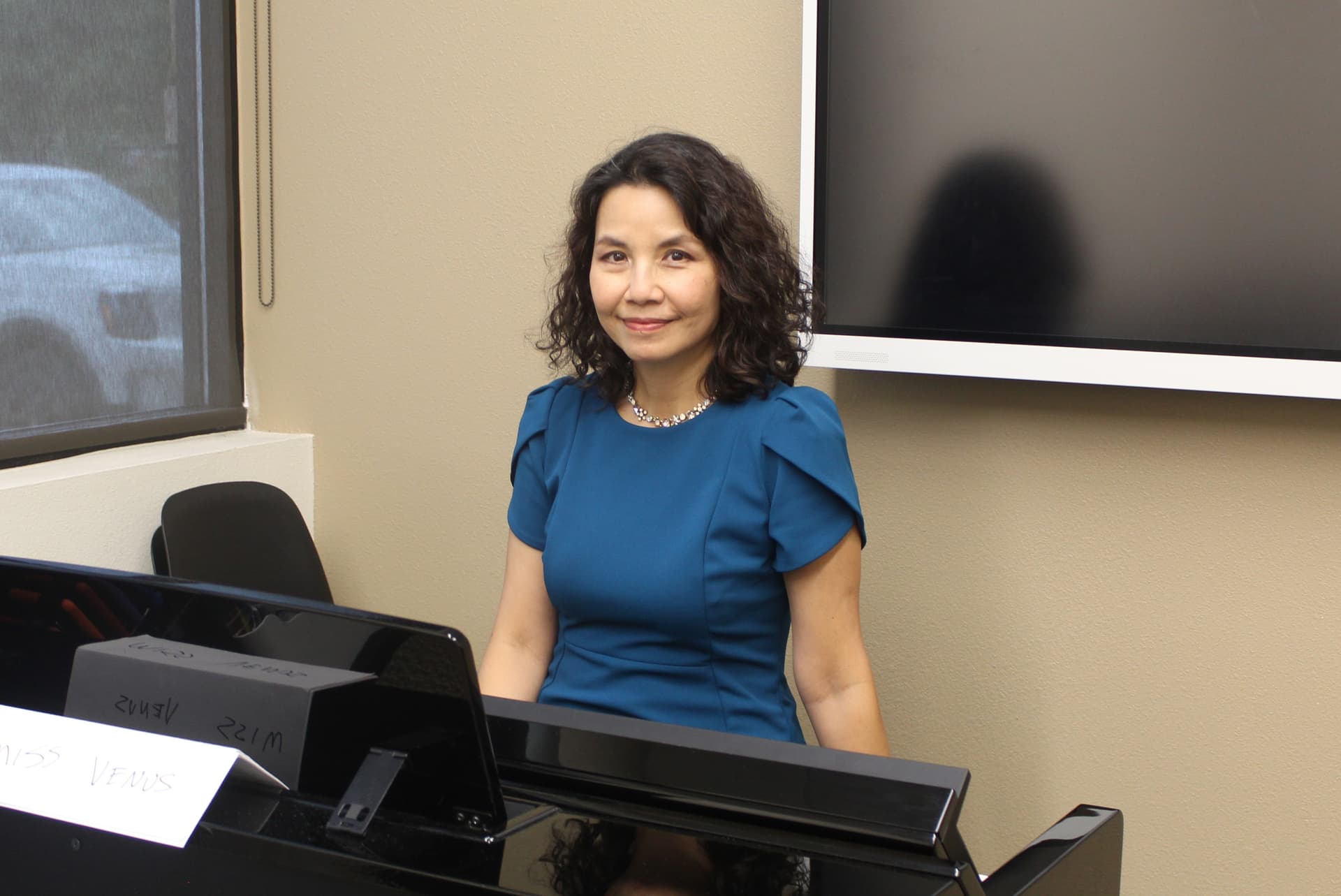 A woman in a blue dress smiles from behind a piano