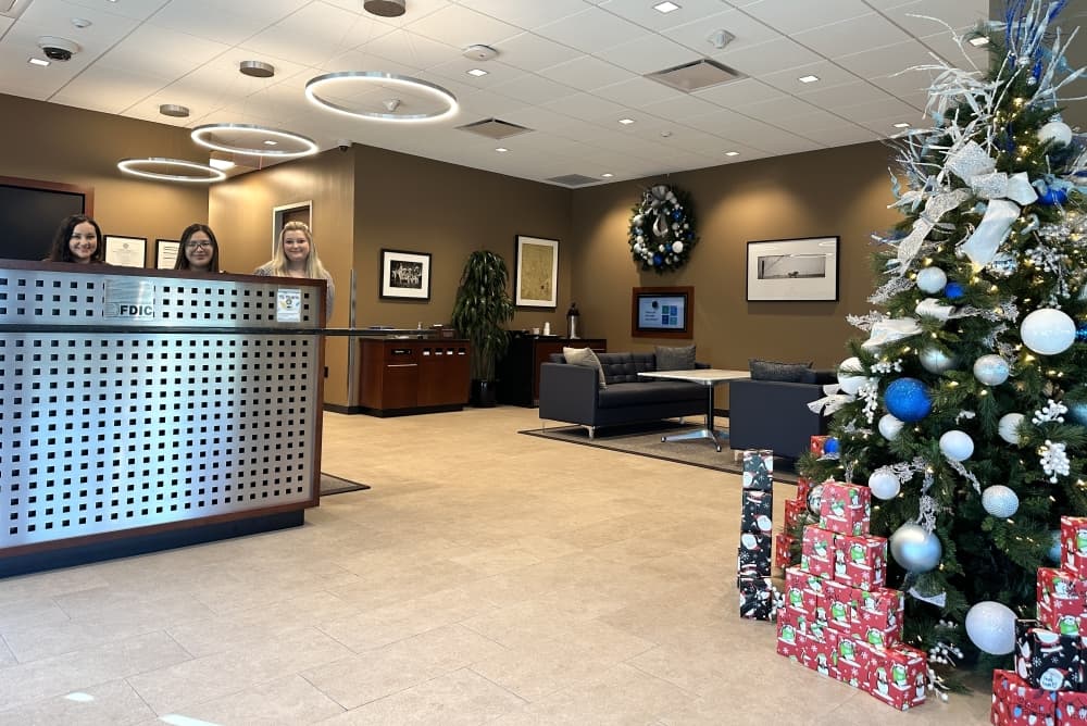 The inside of the lobby is shown decorated for Christmas with three tellers smiling in the photo.