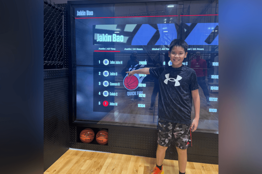 Youth basketball player at Shoot 360 Austin standing in front of interactive leaderboard display showcasing high scores and performance rankings.