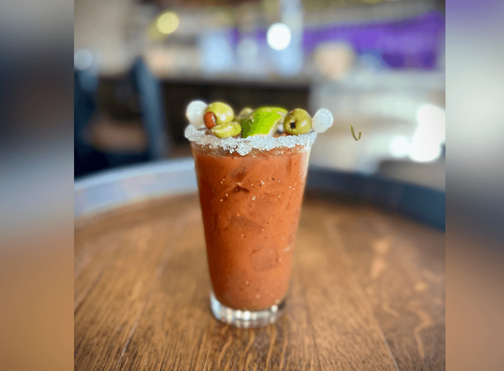 Refreshing Bloody Mary cocktail garnished with celery, olives, and spices, served during Uncork’d Wine Bar & Grill brunch.