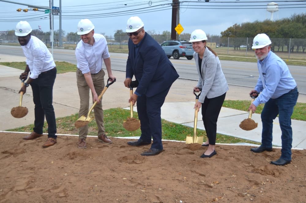 People wear construction hats and dig up dirt