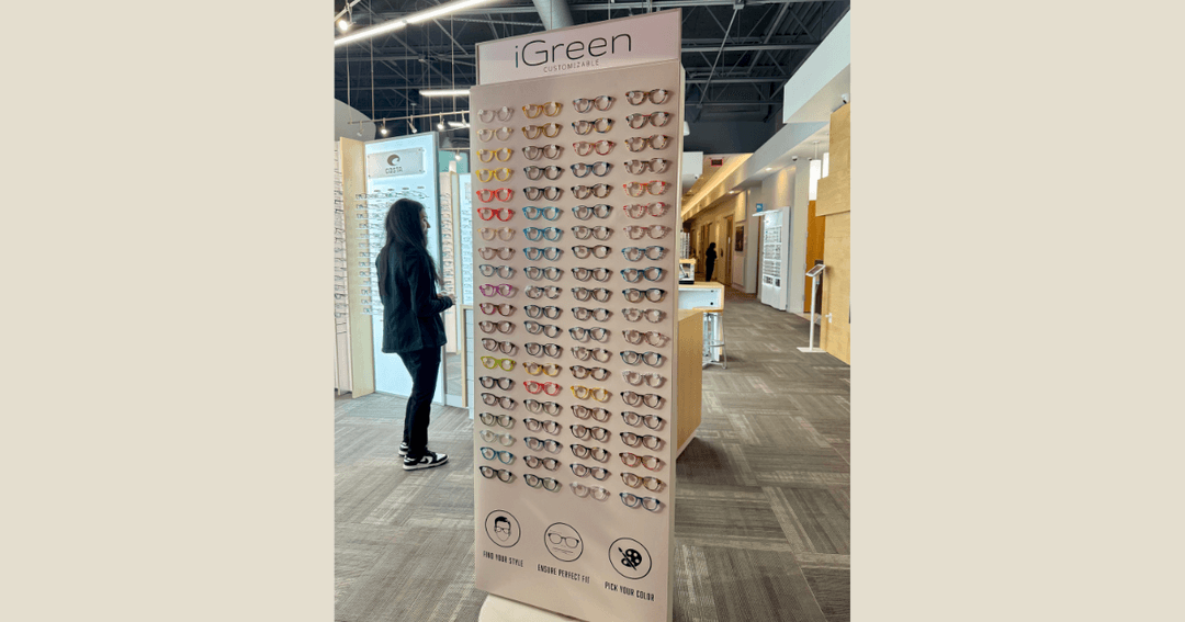 Person browses a tall iGreen eyeglass display with colorful frames inside an optical store.