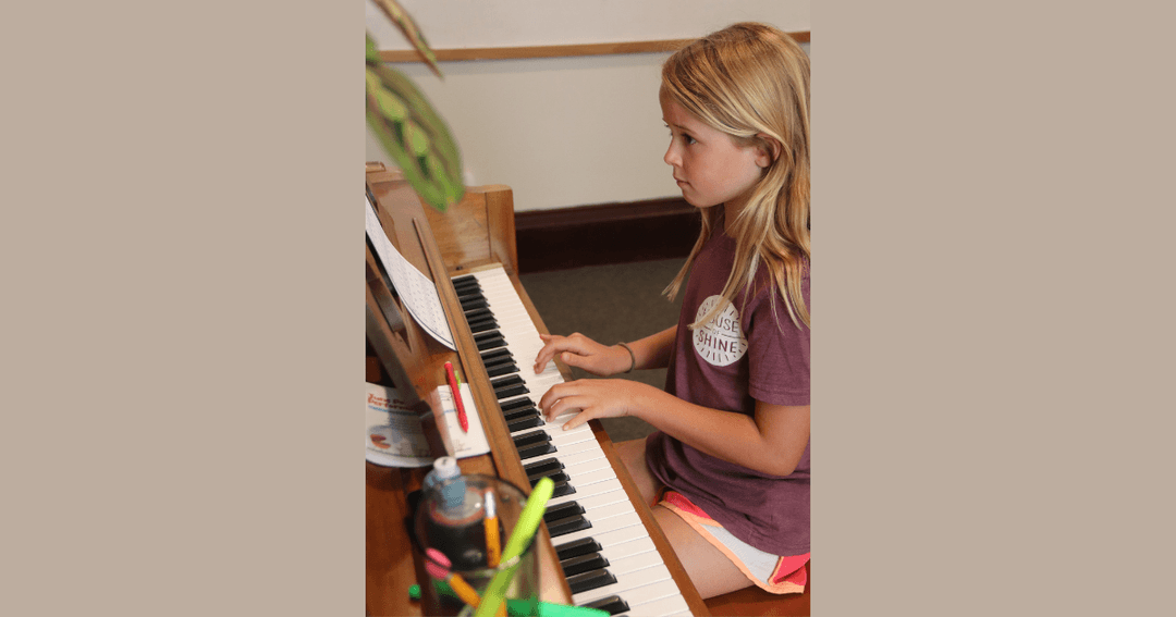 Young girl with blonde hair plays an upright piano while reading sheet music.
