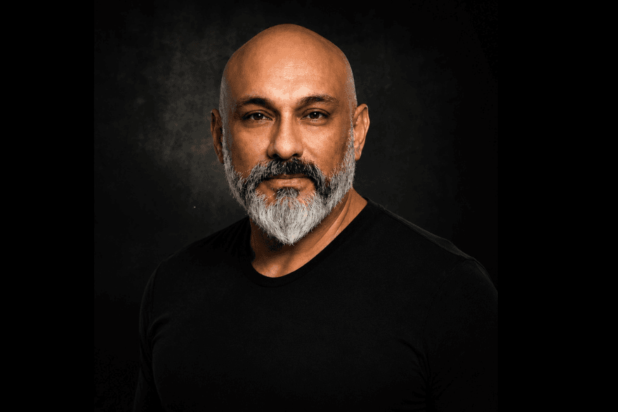 Bald man with gray beard in a black shirt against a dark background, studio portrait.