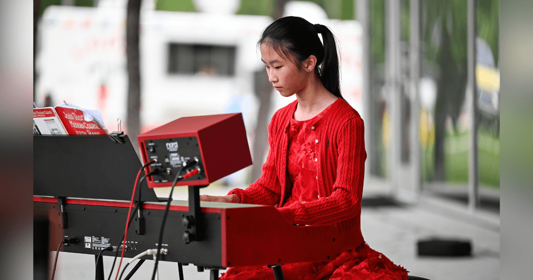 Young girl in red cardigan playing an electronic keyboard outdoors.