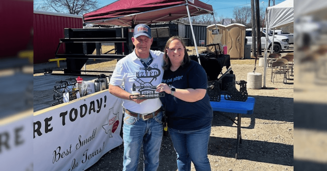 A man and woman hold a chili cook-off trophy at an outdoor event with tents and a banner reading "Best Small in Texas.