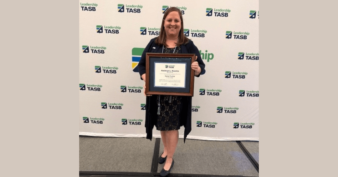 Woman holds framed certificate in front of a Leadership TASB backdrop.