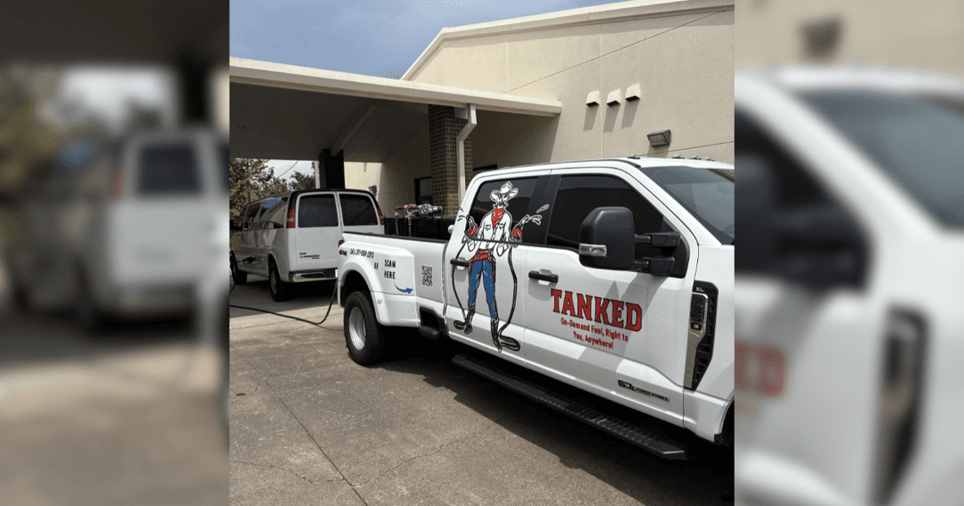 White pickup truck branded "TANKED" with cowboy graphic, refueling a white van parked outside a building.
