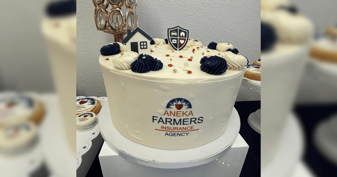 White cake decorated with "Aneka Farmers Insurance Agency" logo, house and shield toppers, navy and white frosting.
