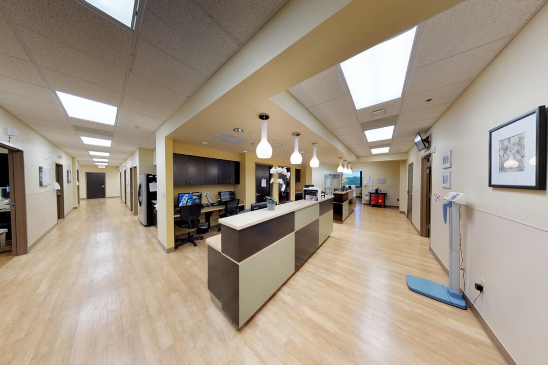 Medical office reception area with a nurses' station, computer desks, hallways with patient rooms, and framed wall art.