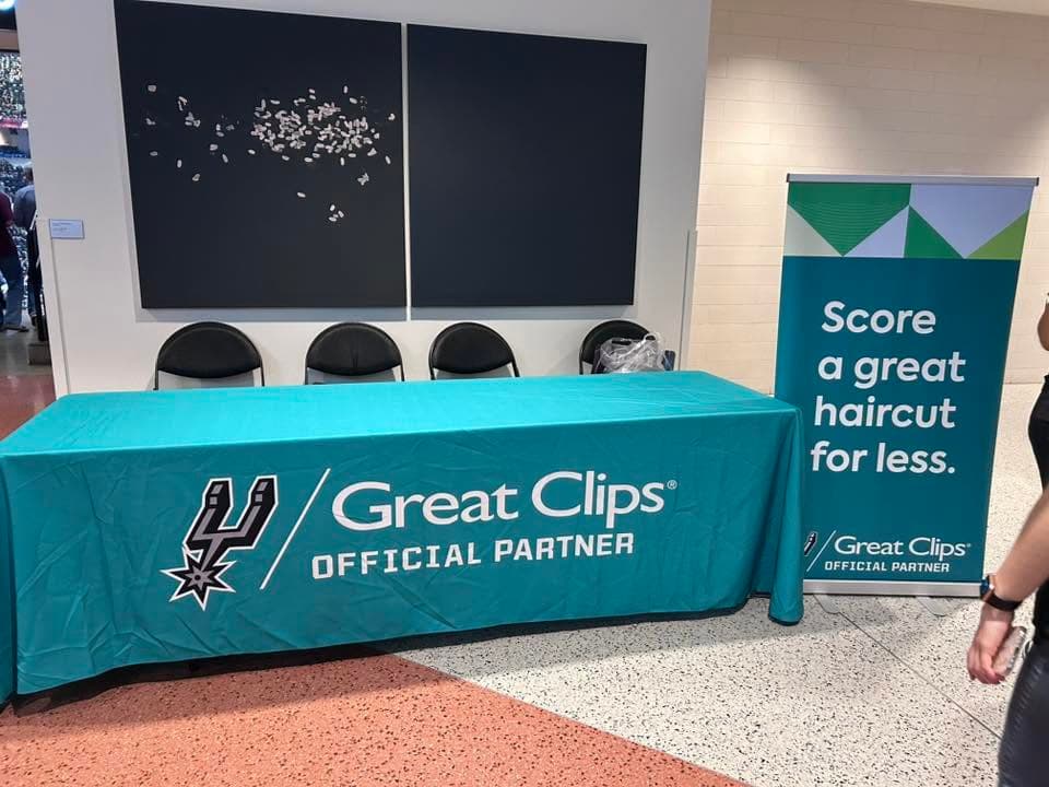 Great Clips promotional table with Spurs logo and banner reading "Score a great haircut for less" at an arena.