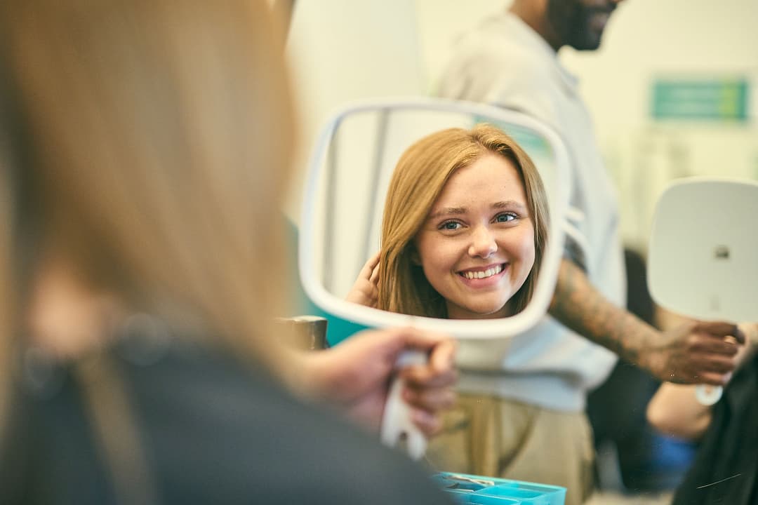 Smiling woman admiring her new hairstyle in a hand mirror at a salon.