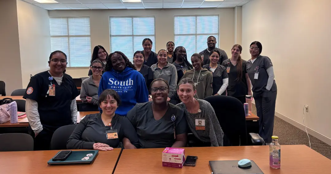 Group of smiling students in scrubs, one in a South University Austin sweatshirt, posing together in a classroom.