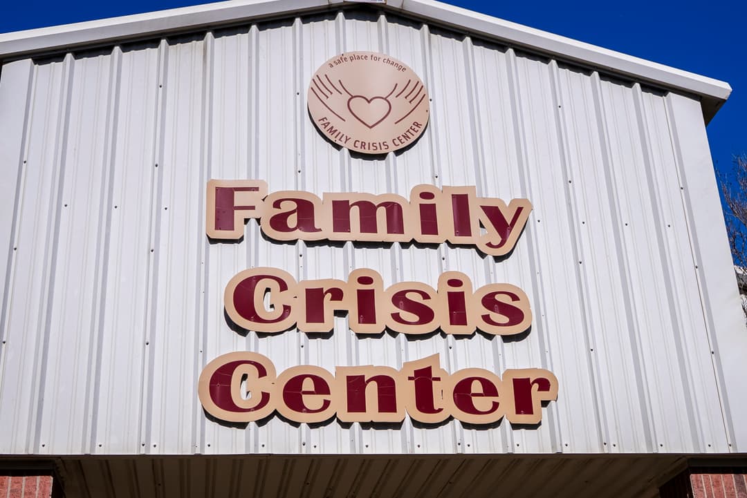Family Crisis Center" signage with heart-and-hands logo on a white metal building against a blue sky.