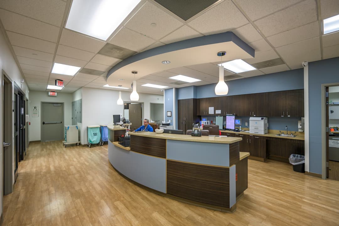 Medical clinic nurses' station with curved reception desk, computers, and a staff member seated behind it.