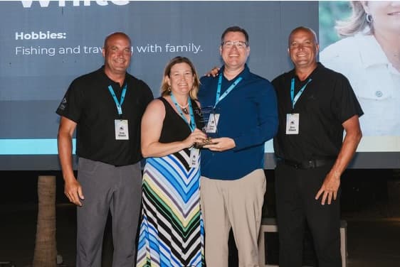 Four people pose on stage, a couple in center holding a glass award, at an awards event.