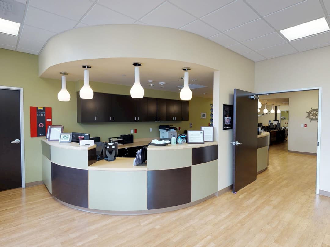 Curved reception desk in modern office lobby with pendant lights, dark cabinets and open doorway to back rooms.