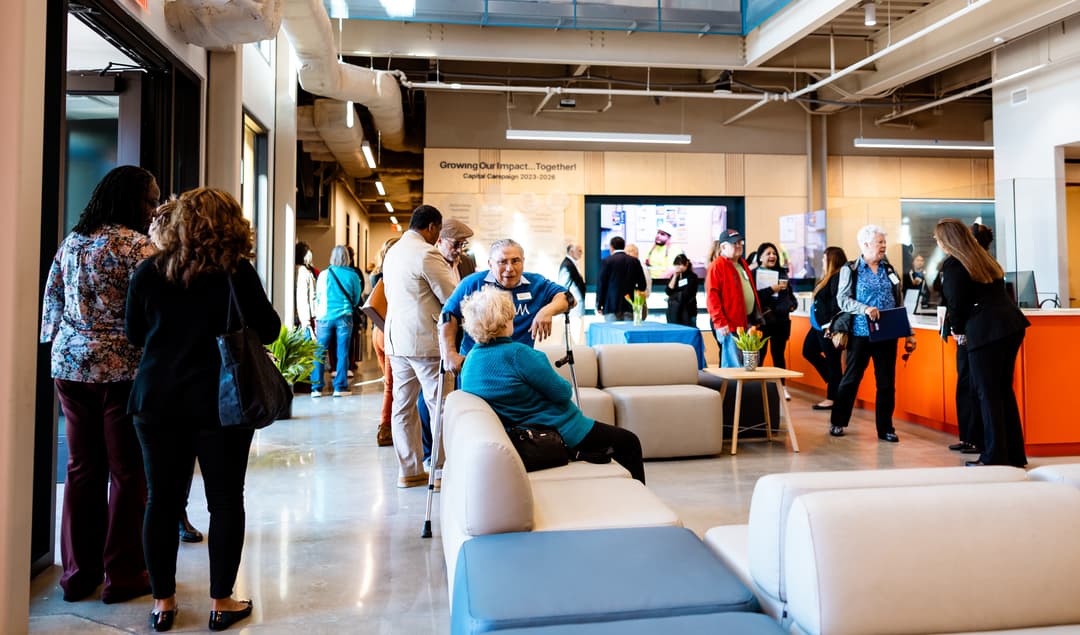 People mingle in a modern lobby with a "Growing Our Impact...Together! Capital Campaign 2023-2026" wall sign.