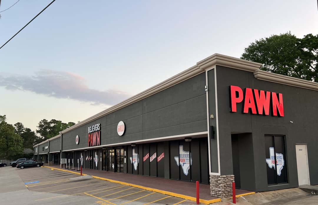 Exterior of Believers Pawn shop in Tomball, Texas, with large red PAWN sign and empty parking lot at dusk.