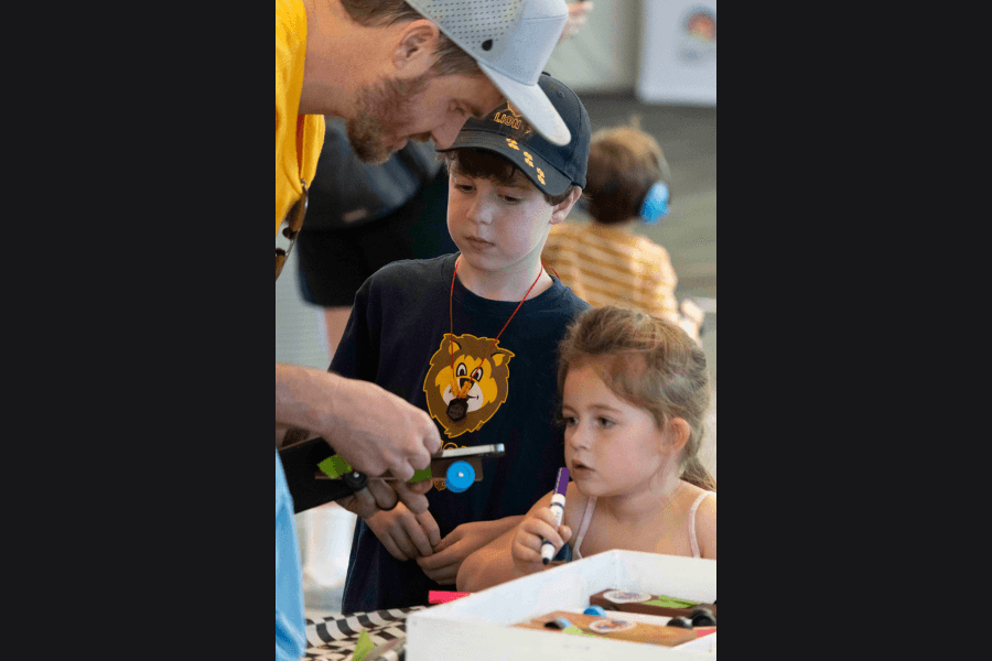 Man helps a boy and girl with a craft project at a table during a hands-on activity event.