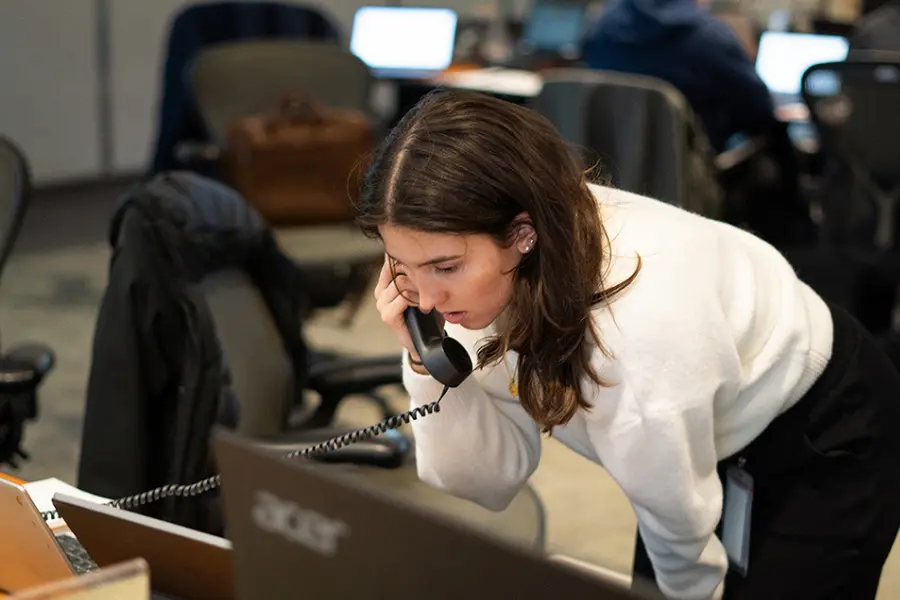 Woman in white sweater talks on a corded phone while looking at an Acer laptop in an office.