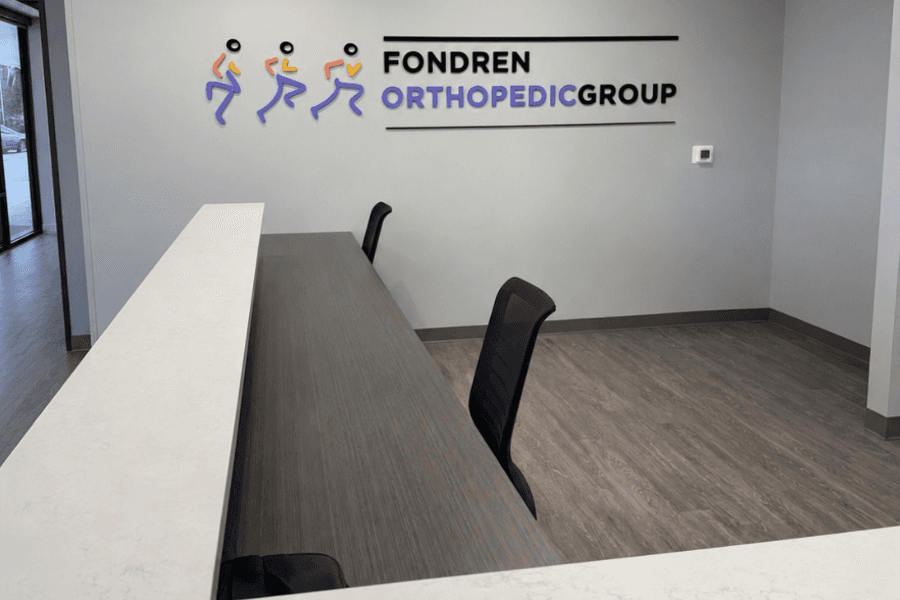 Fondren Orthopedic Group reception desk with logo of running figures on wall above empty check-in counter.