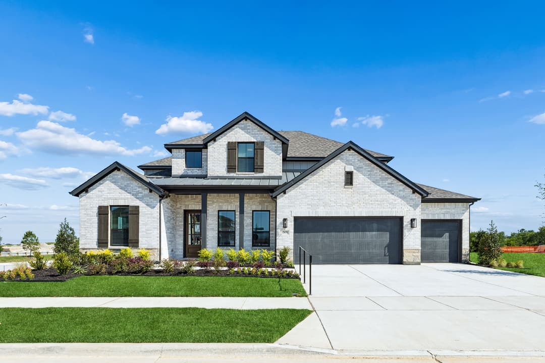New two-story light brick home with three-car garage, manicured lawn and landscaping under blue sky.