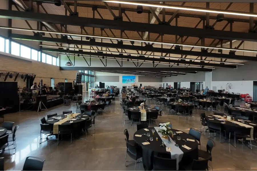 Large event hall with round tables set for dining and a stage with band setup at left.