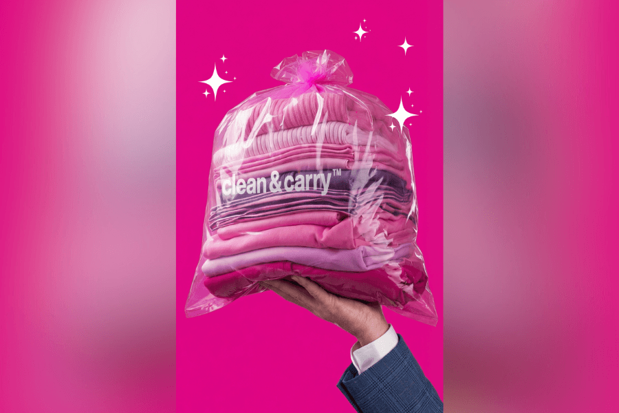 Hand holding a clear "clean & carry" bag of folded pink laundry against a hot pink background with sparkles.