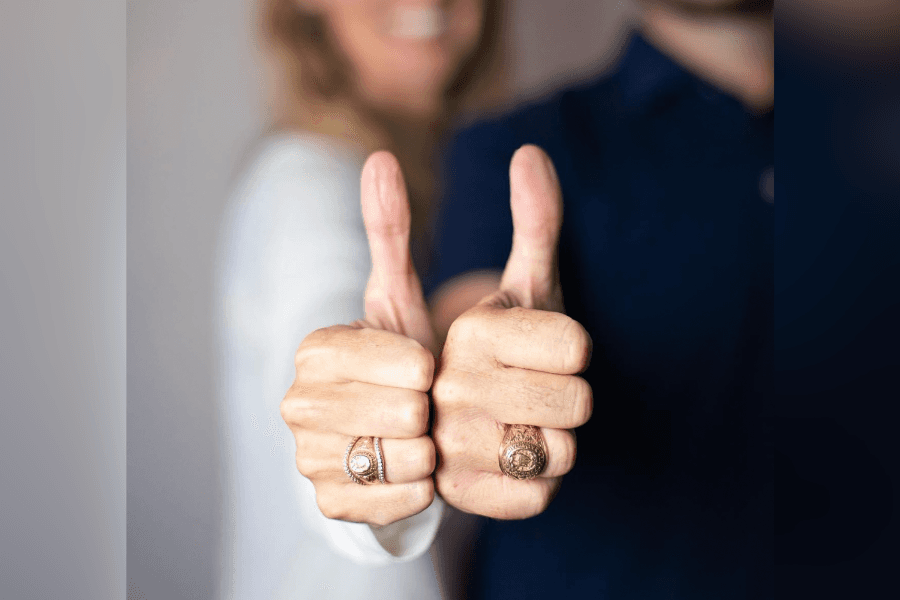 Two people give thumbs-up, showing off gold rings on their fingers.
