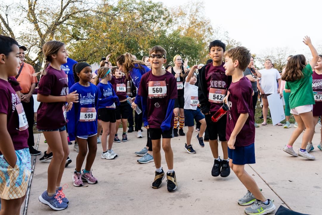 Children wearing race bibs gather with adults before a Turkey Trot 5K run outdoors on a paved path.