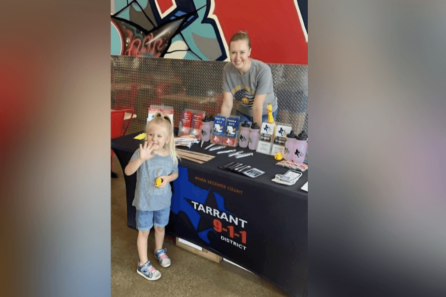 Young girl and woman at a Tarrant 9-1-1 District information table with promotional items and brochures.