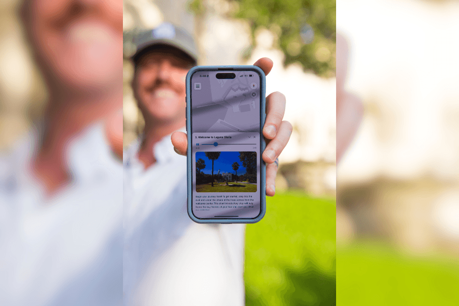 Smiling man holds up smartphone displaying a Laguna Gloria audio tour app with a map and photo.